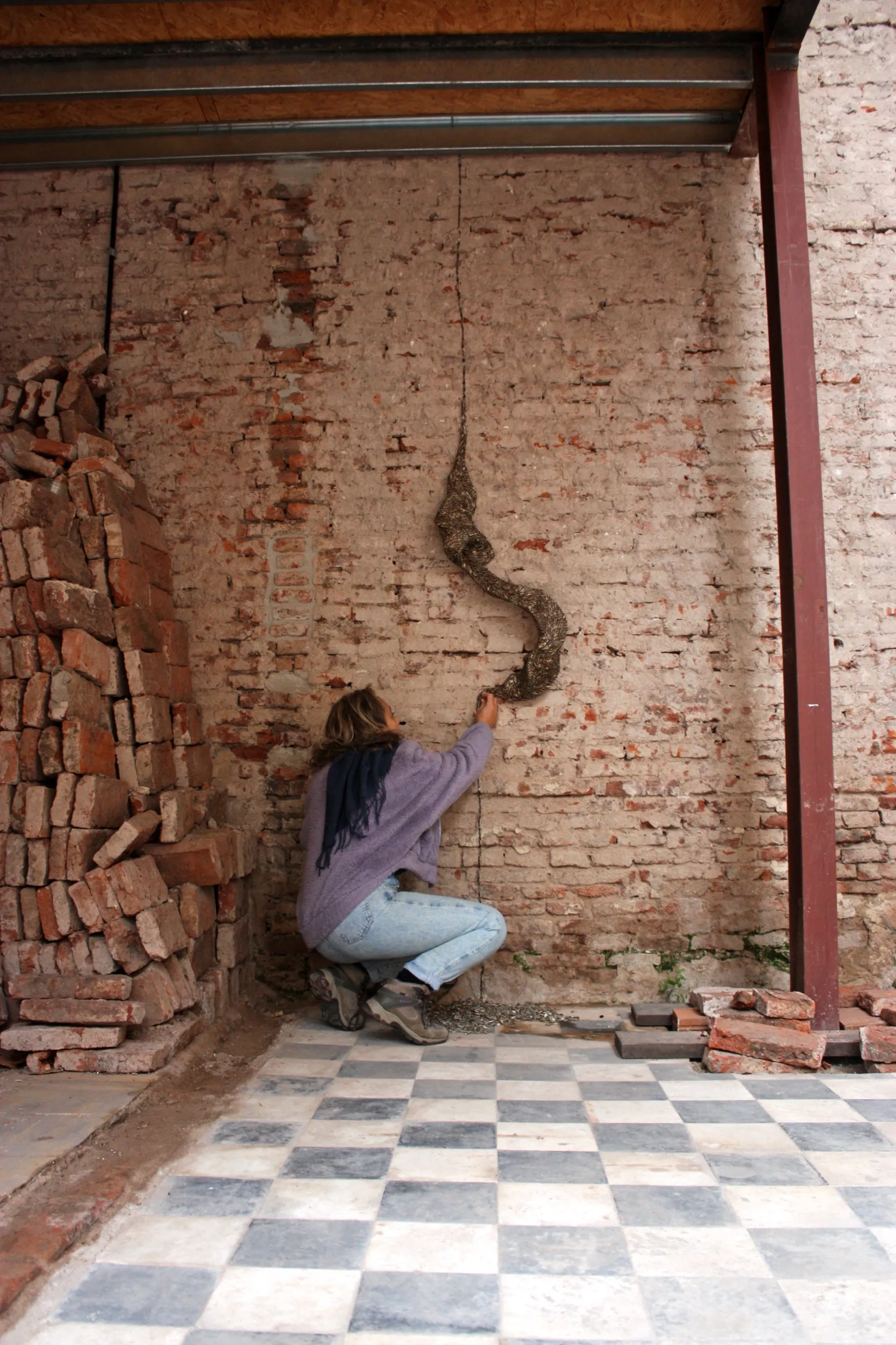 Luciana Fernández montando una obra de la serie de semillas sobre una pared de ladrillos